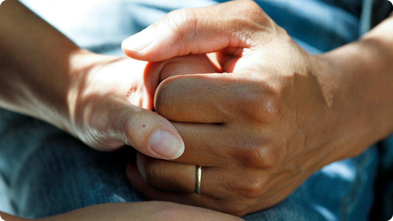 A close-up shot of a couple’s intertwined hands in support of each other. 