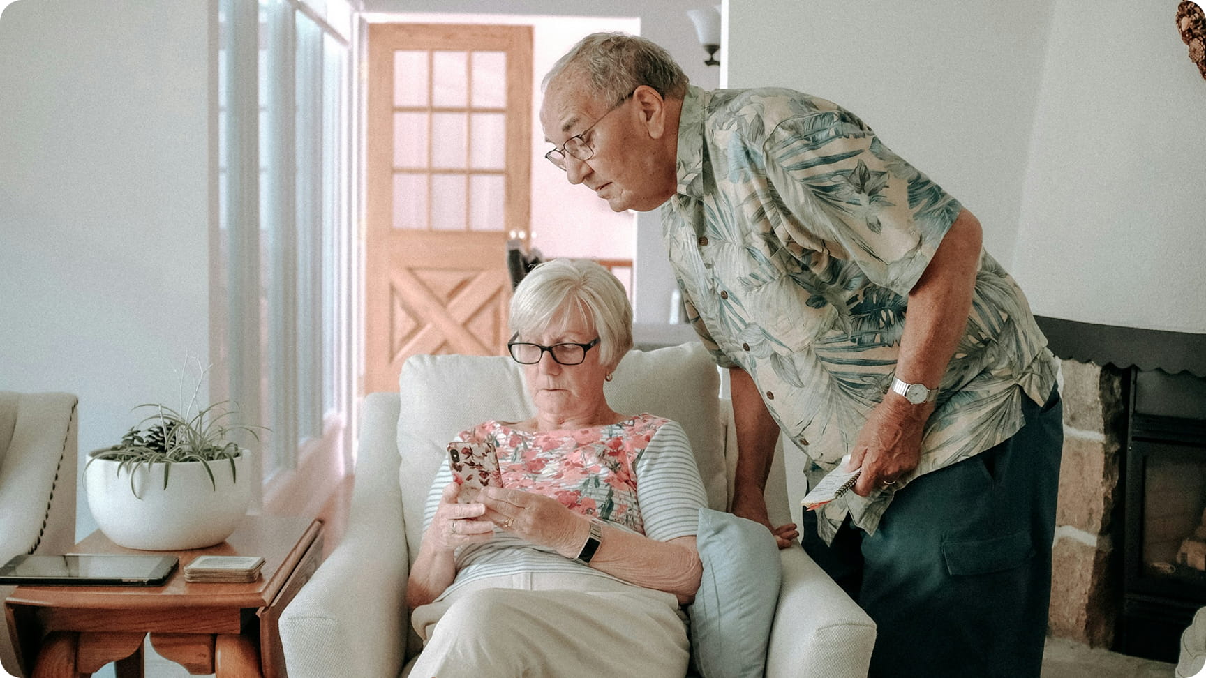  An older couple browsing on a cellphone in their living room.