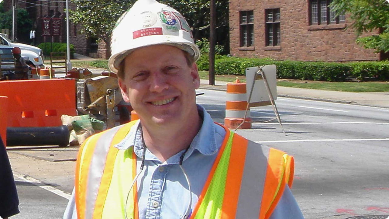 George wearing a hard hat and safety vest at a construction site.