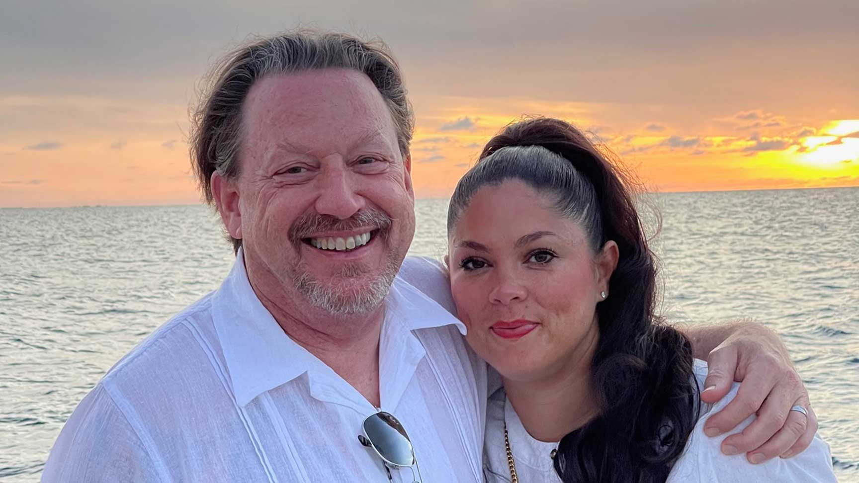 George and his wife smiling together on a sunny beach.