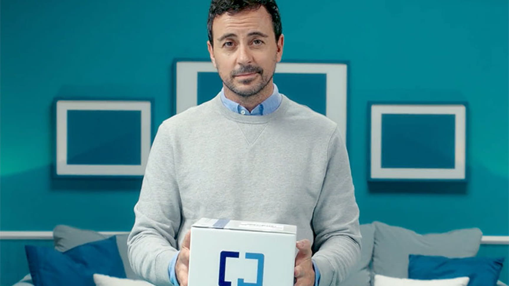 A man holds a Cologuard box in his living room.