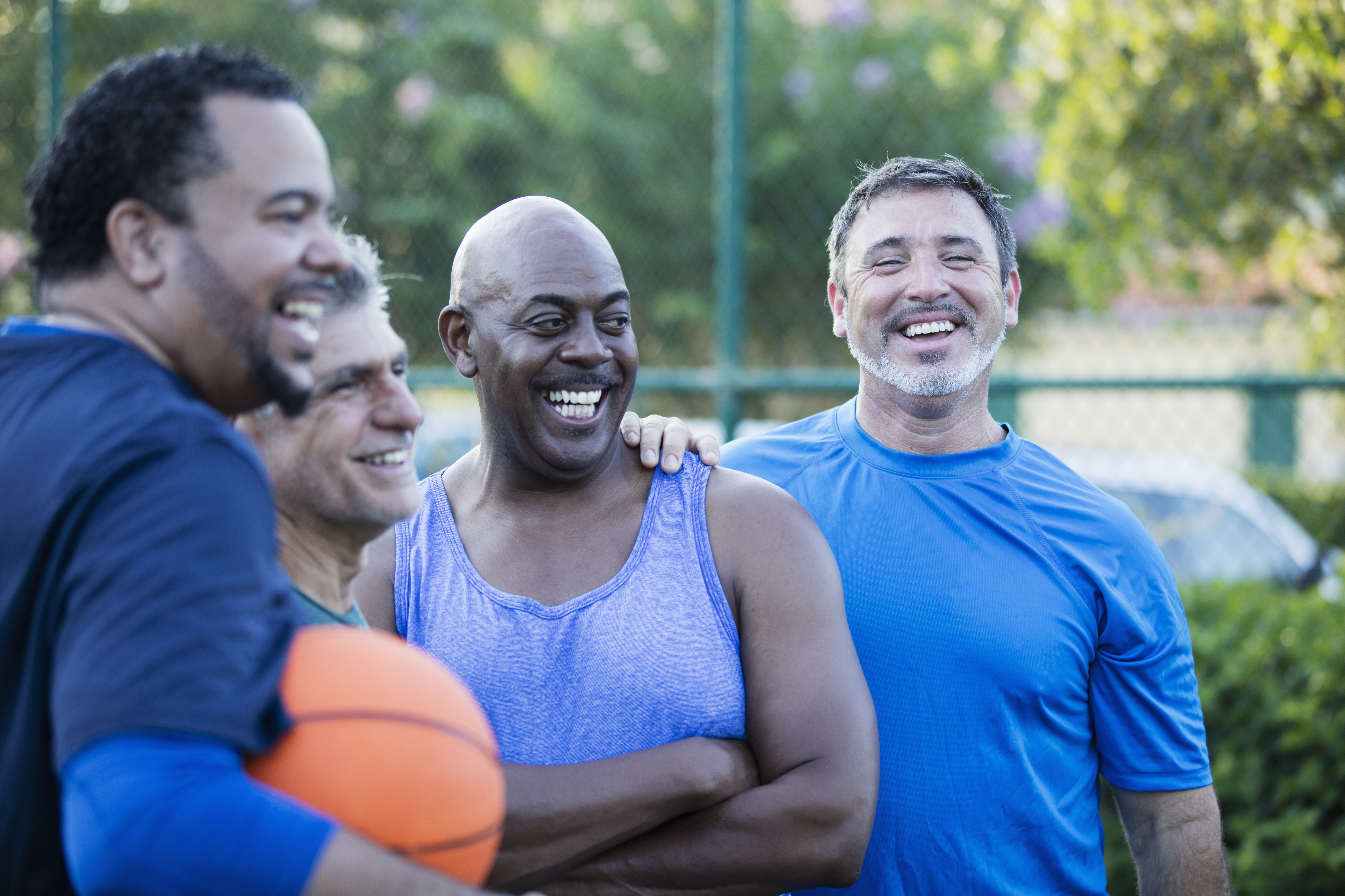 A group of men wearing blue shirts take a break from a game of basketball.