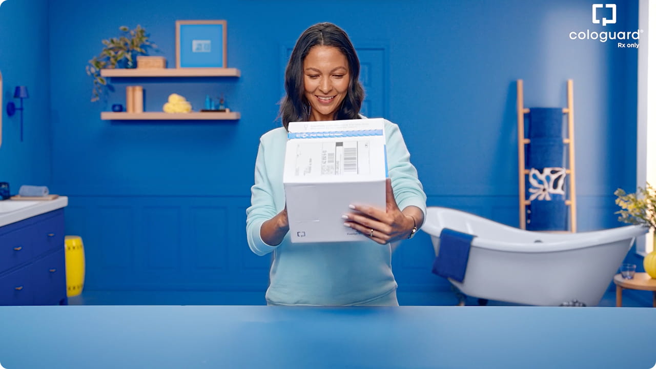  A woman stands in her bathroom holding a Cologuard box.