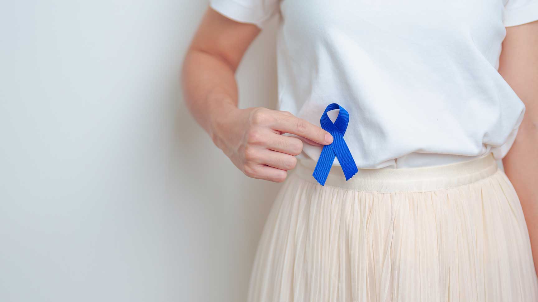 A woman holds a blue ribbon near her abdomen in honor of Colorectal Cancer Awareness Month.