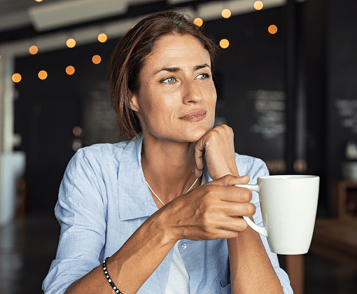 Woman looking thoughtful while holding coffee — emphasizing health reflection and screening.