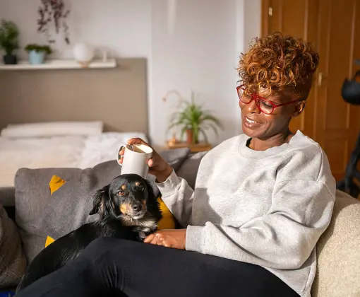 A woman holding a coffee mug and sitting on a sofa next to a dog