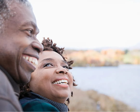 A man and woman smile at each other by a lake.