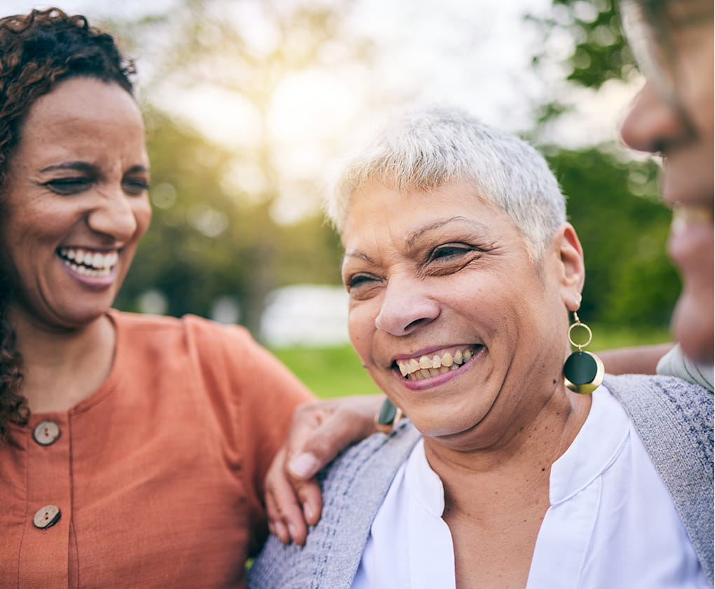 A mother and daughter standing outside on the grass smiling at each other.