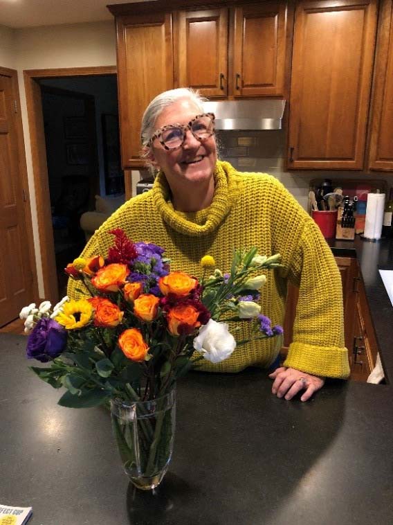 Lynn, a patient who screened with Cologuard, standing behind a counter with a vase of flowers placed on the counter top