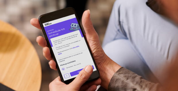 A cellphone in a person’s hands with a screen displaying a kit pickup scheduling application