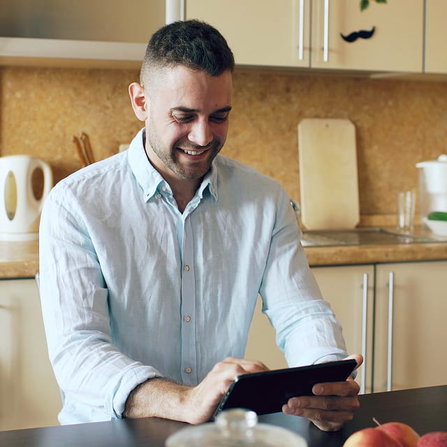 A man sits in his kitchen while using a tablet.