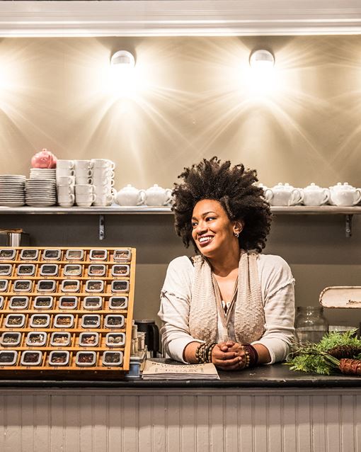 A smiling woman standing behind the counter at a tea shop.