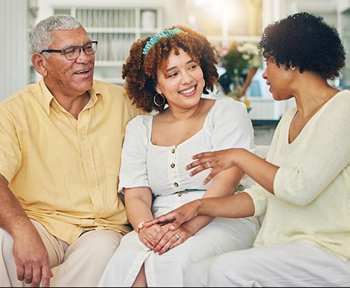 Una mujer adulta tiene una amena conversación con familiares mayores que ella en un hogar lleno de luz y decorado con flores.