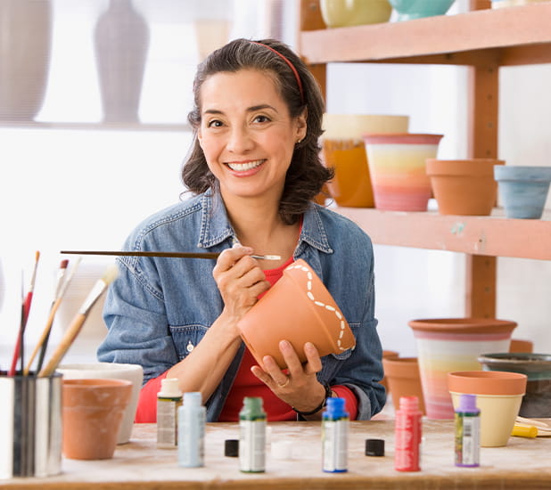 Una mujer en un taller de cerámica está contenta con la vasija que adorna con un pincel.  